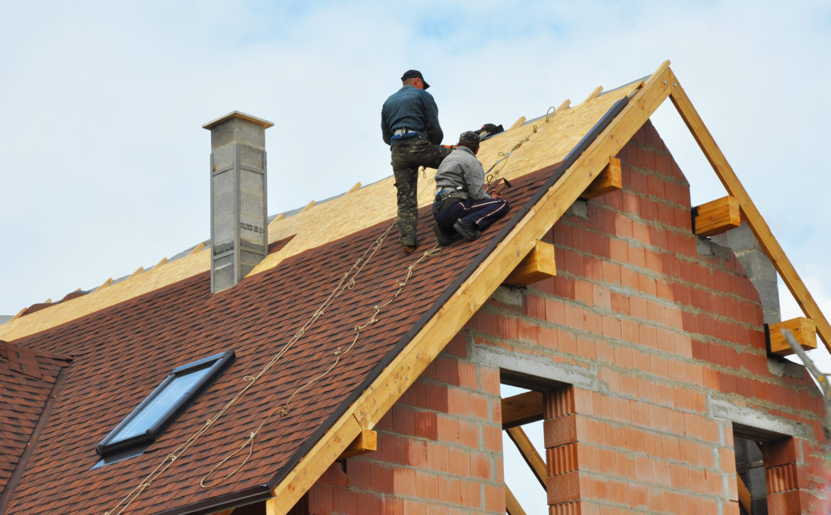 Roofing Construction and Building New Brick House with Modular Chimney, Skylights, Attic, Dormers and Eaves Exterior. Roofers Install, Repair Asphalt Shingles or Bitumen Tiles on the Rooftop Outdoor.